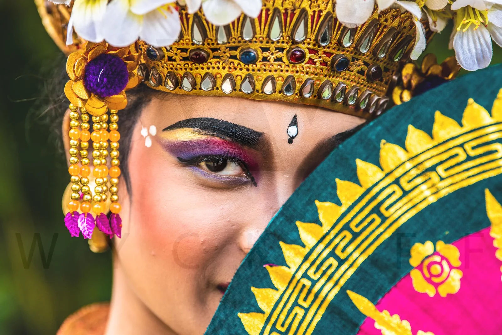 A performer in an ornate gold headdress peers over a patterned fan