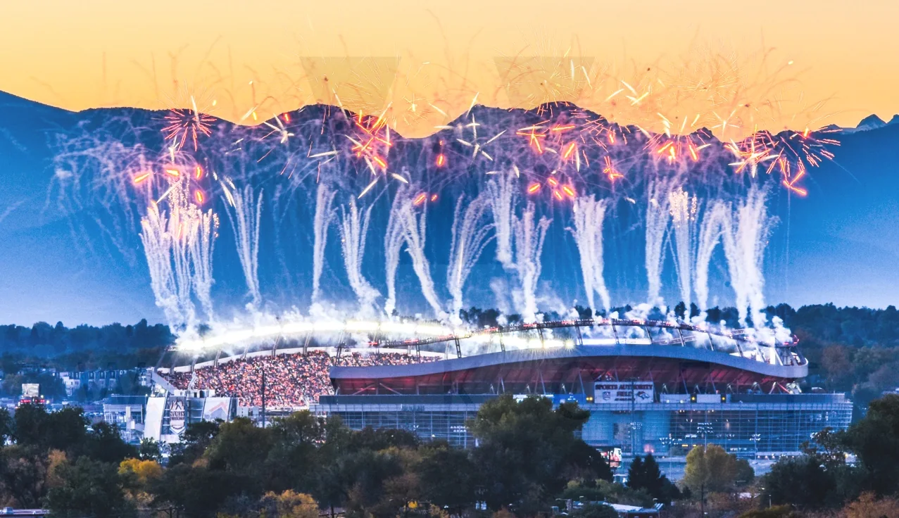 Fireworks burst above a packed stadium at dusk