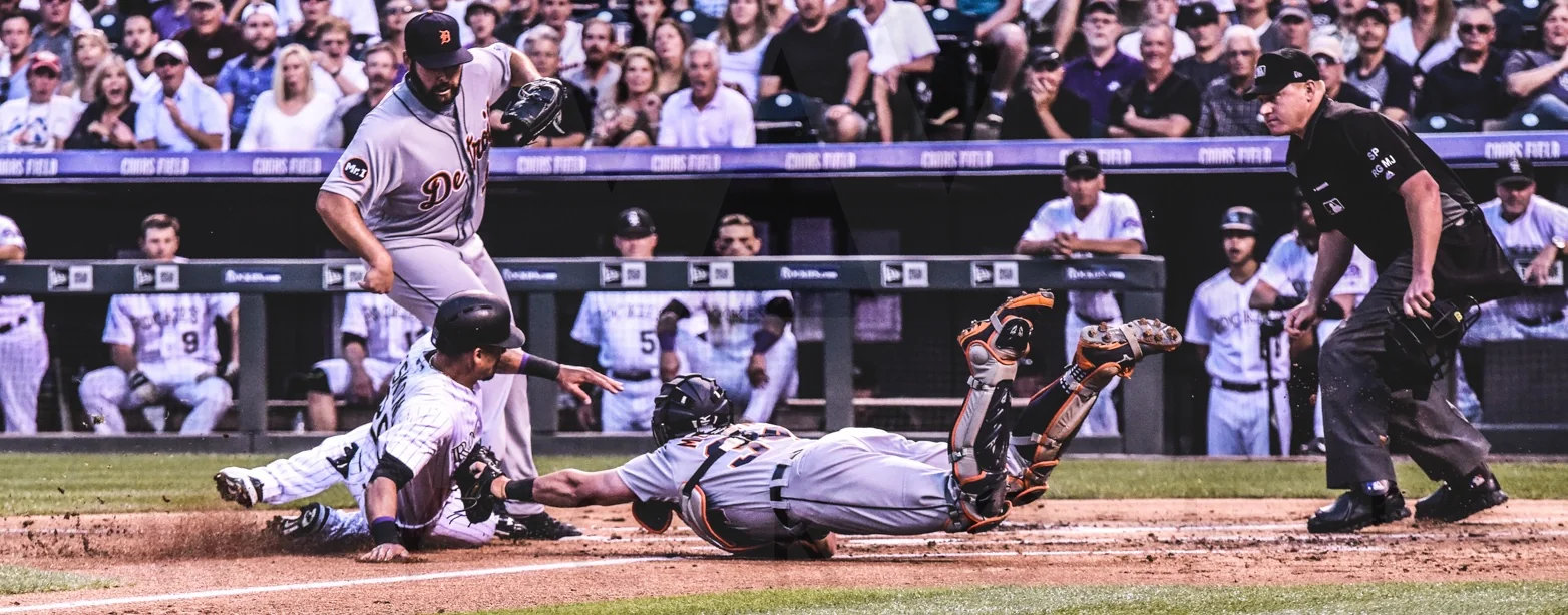 A baseball runner slides toward home plate as the catcher reaches for the tag
